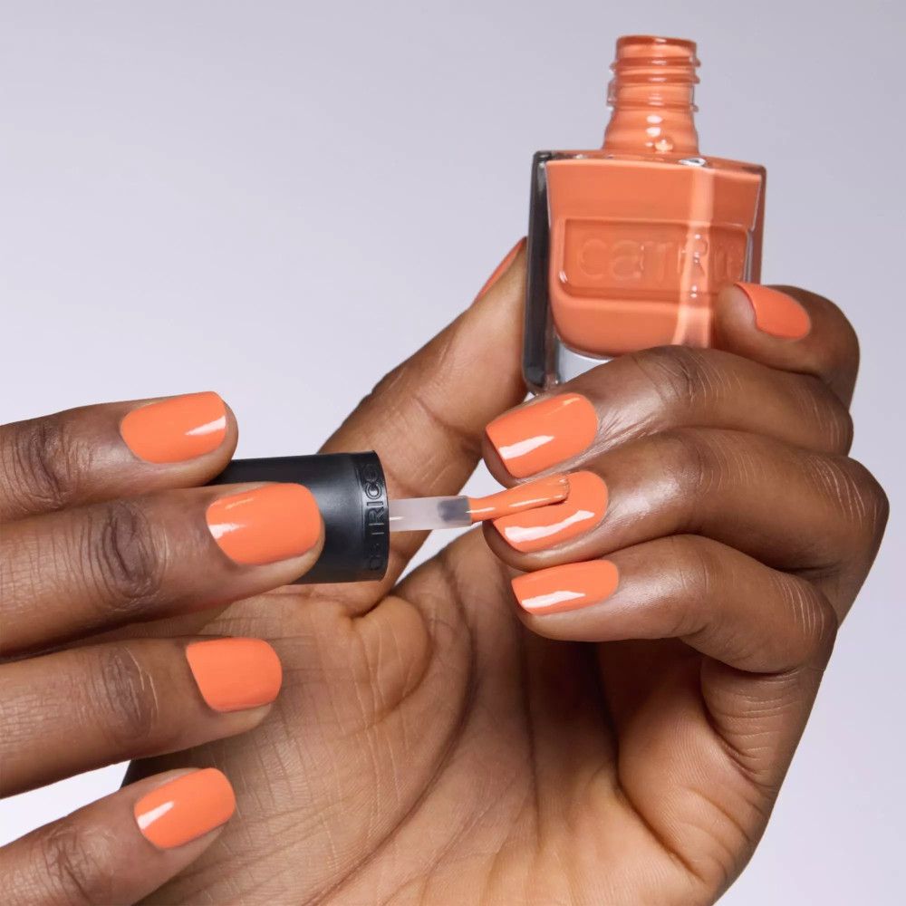 Main avec ongles vernis et flacon de vernis. Utilisation du pinceau. Couleur : orange.