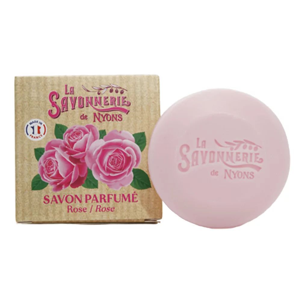 Ronde, roze zeep en kartonnen verpakking. Op de verpakking: "La Savonnerie de Nyons", rozenafbeelding, "Savon Parfumé". 