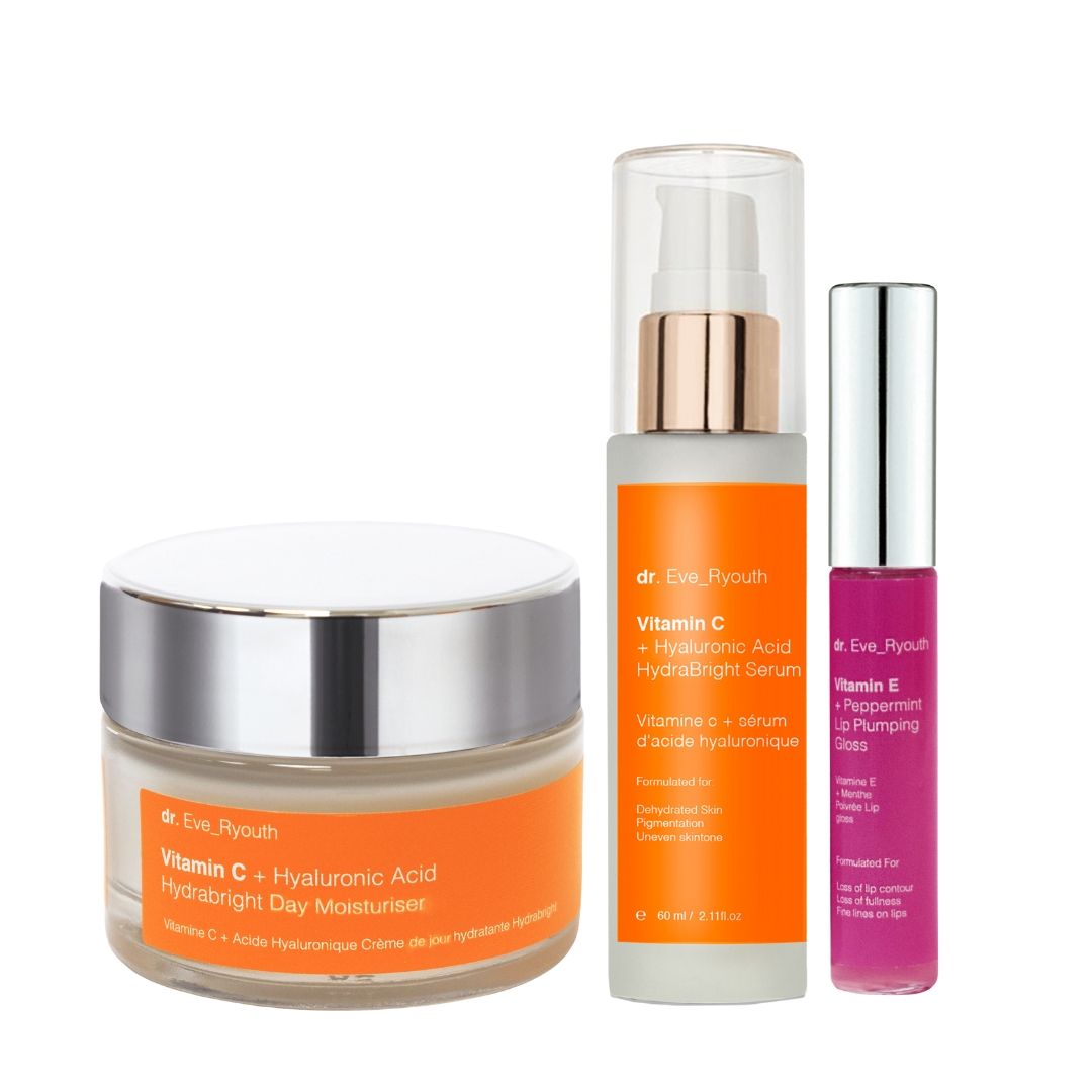 Drie cosmetische producten: crème, serum en lipgloss. Crème- en serumverpakkingen met oranje etiketten. Lipgloss in roze verpakking.