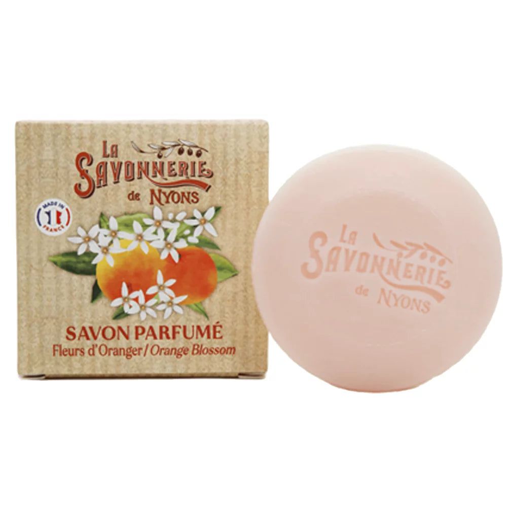 Roze ronde zeep en kartonnen verpakking. Op de verpakking: La Savonnerie de Nyons, illustratie van oranjebloesem en tekst.