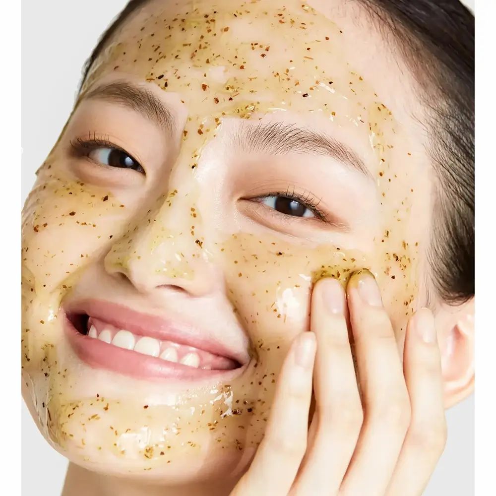 Gezicht met gelmasker. Het masker bevat groene deeltjes. De persoon lacht.