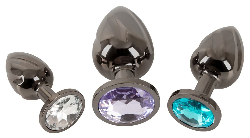Trois plugs anaux en métal avec des pierres précieuses blanches, turquoise et violettes.