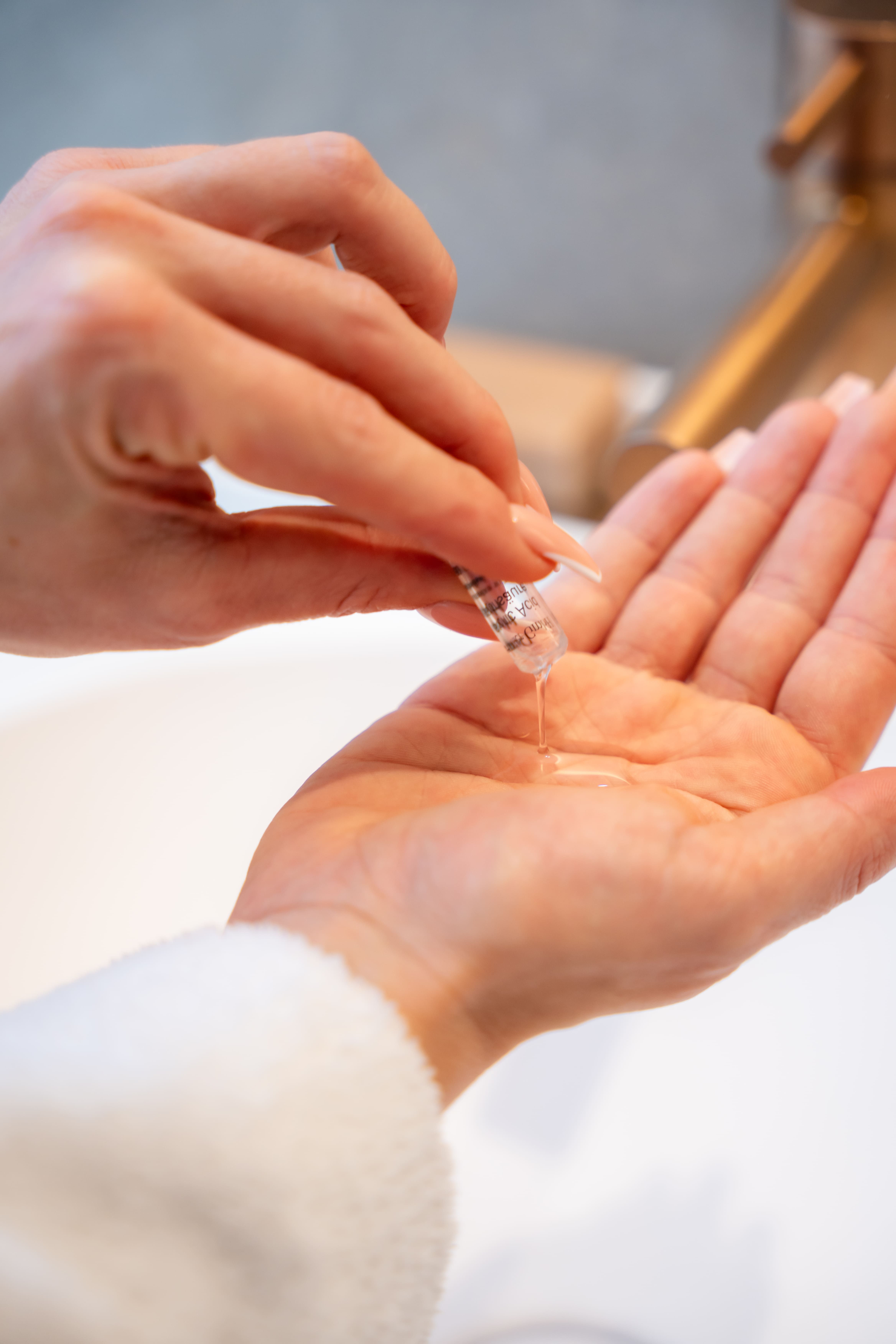Een hand houdt een kleine ampul vast waaruit een heldere vloeistof in de andere hand druppelt.