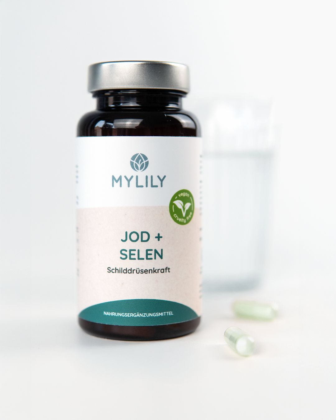Bouteille en verre brun avec des gélules Mylily Iode + Sélénium pour la thyroïde. Deux gélules sont à côté.