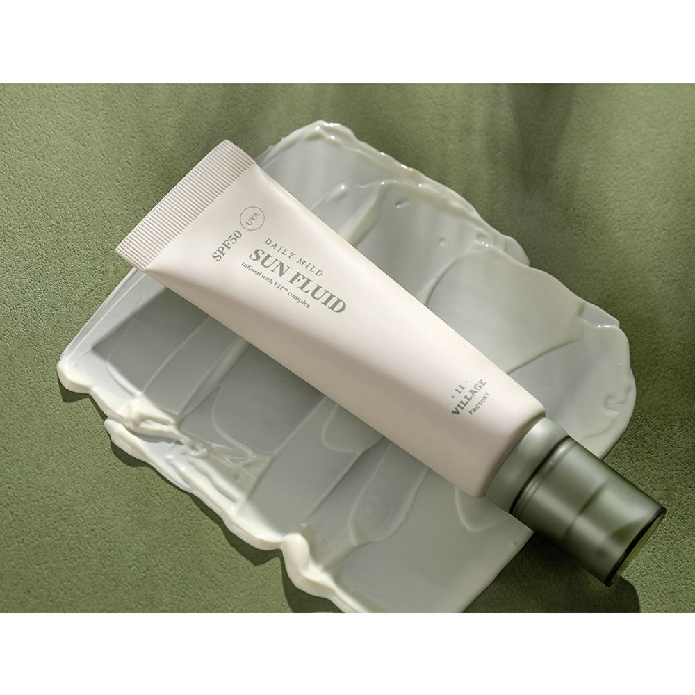 Beige tube op witte crème. Opschrift: SPF50, Daily Mild Sun Fluid, UVA. Merk: Village 11 Factory.