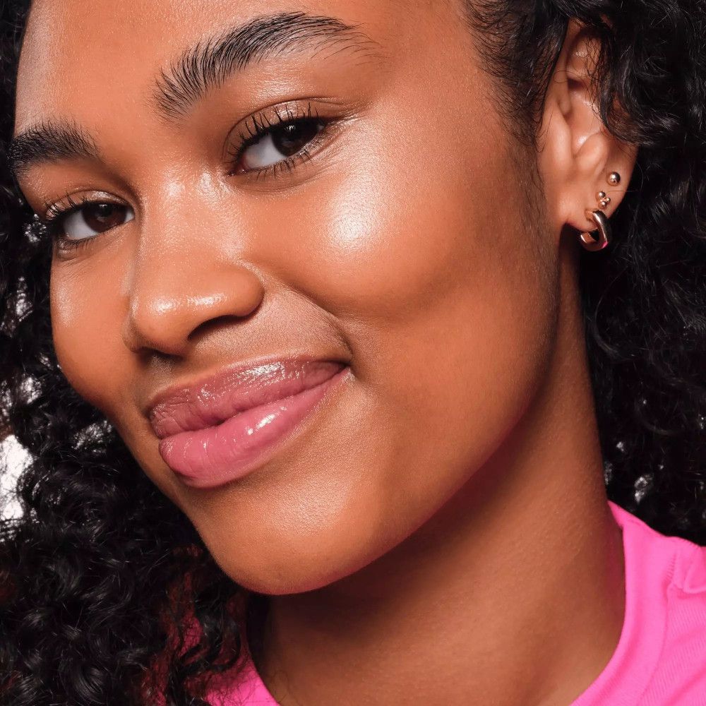 Gros plan sur un visage avec highlighter. Peau foncée, peau brillante. Haut rose.