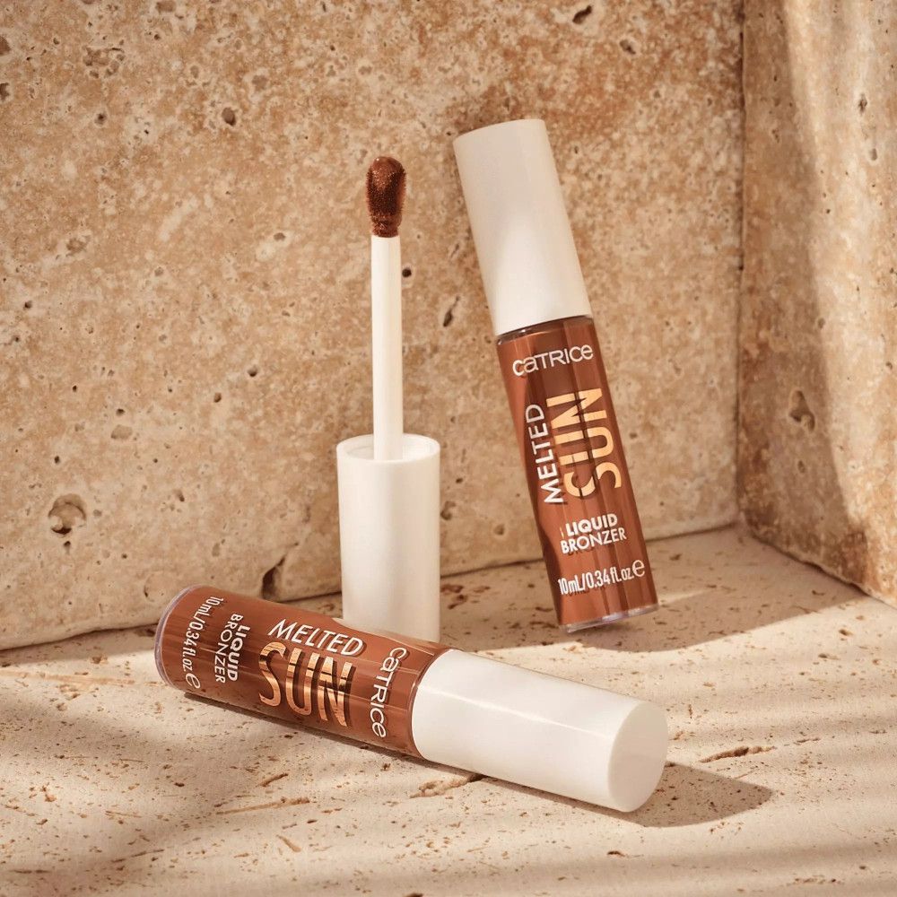 Deux flacons de bronzer liquide avec applicateur. Inscription: Melted Sun, Liquid Bronzer. Fond: mur de pierre beige.