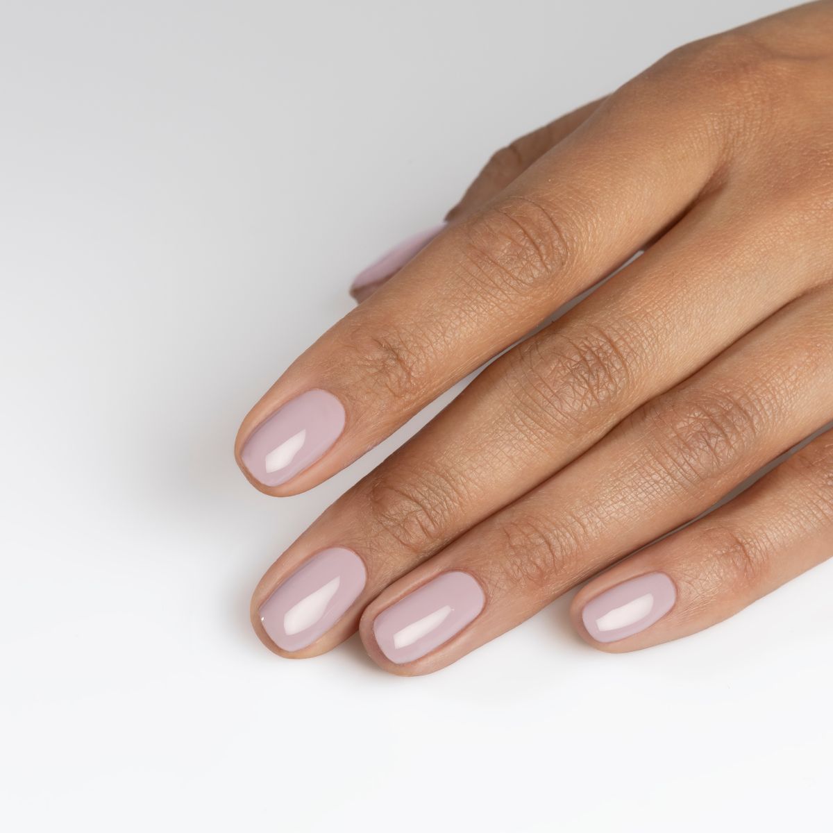 Main avec ongles roses clairs ovales. La main est posée sur fond blanc.