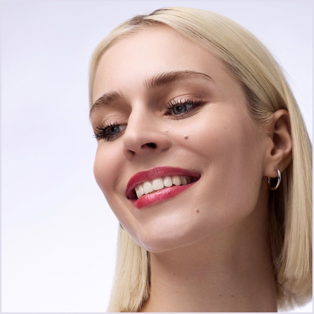 Portrait d'une femme souriante avec du rouge à lèvres. Les lèvres sont remplies d'un remplisseur de lèvres rose.