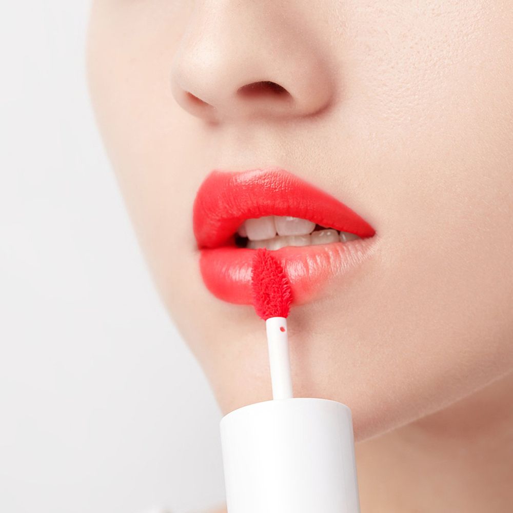 Application de rouge à lèvres rouge sur les lèvres. L'applicateur est visible. Les lèvres sont rouges.