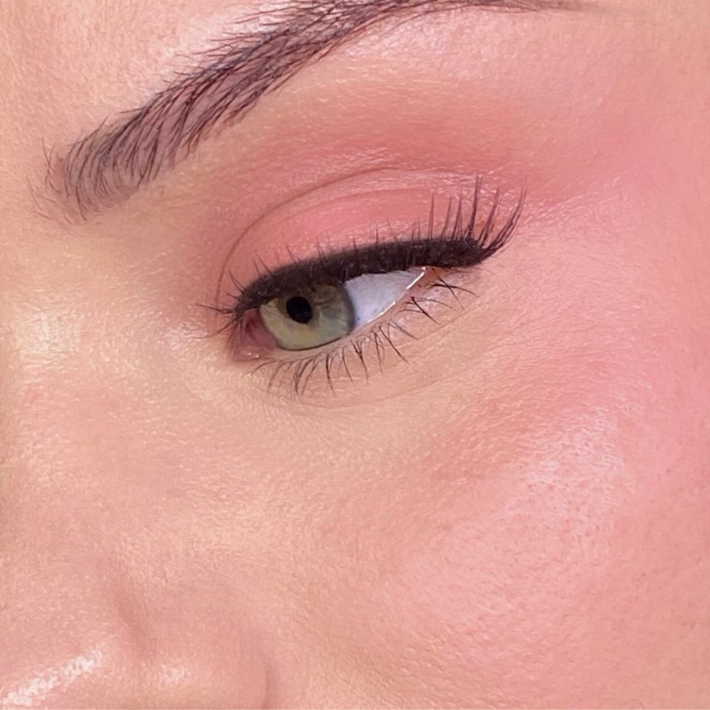 Gros plan d'un visage maquillé de rose sur les yeux et les joues. Œil vert, eye-liner noir.