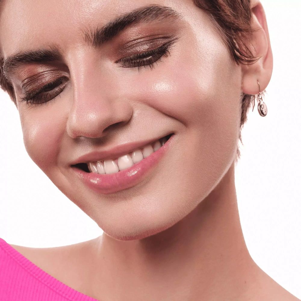 Femme avec de l'ombre à paupières crème sur les yeux. Elle sourit. Haut rose.