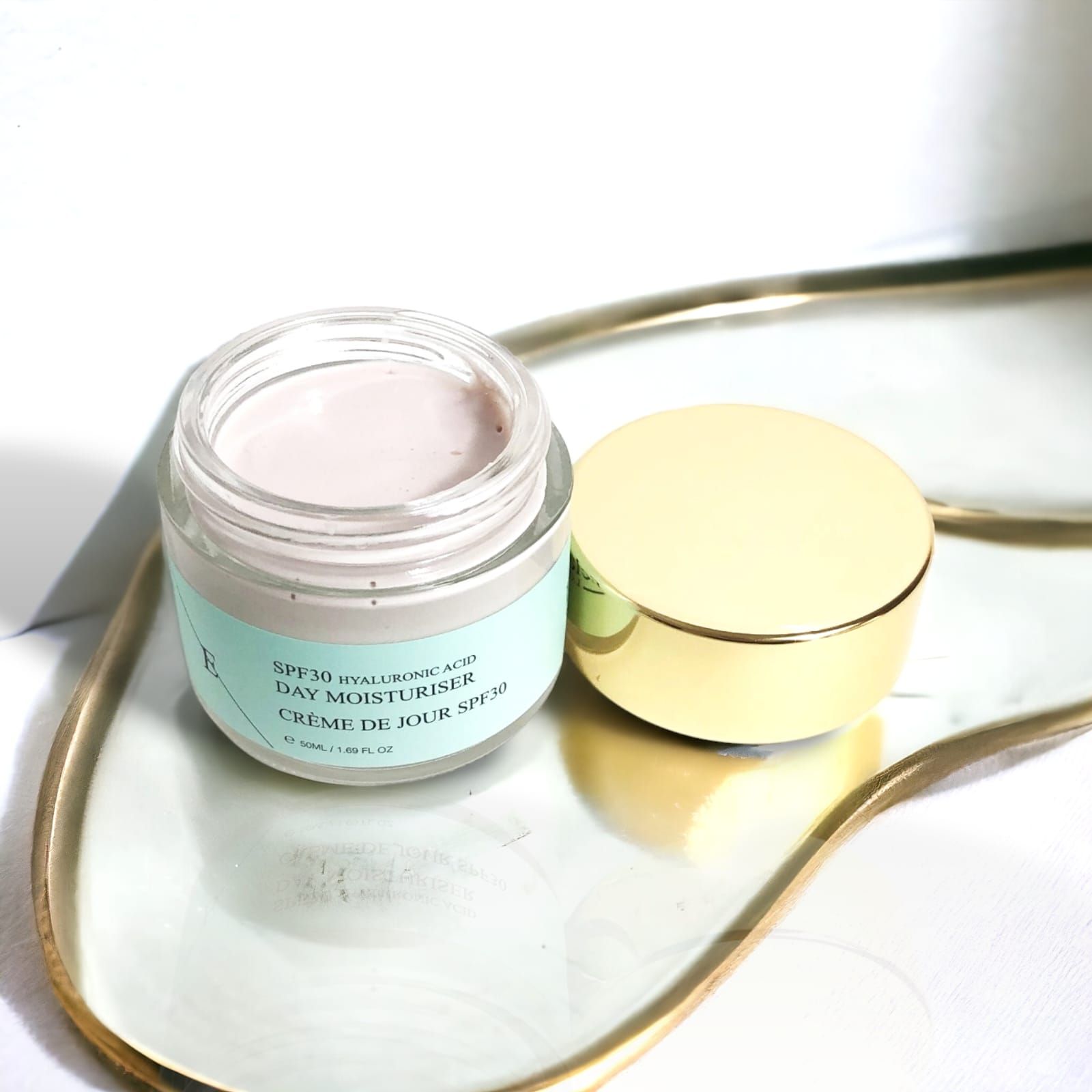 Pot de crème de jour avec couvercle doré, ouvert, sur un plateau. Inscription : SPF30 Acide Hyaluronique Day Moisturiser Crème de Jour SPF30.