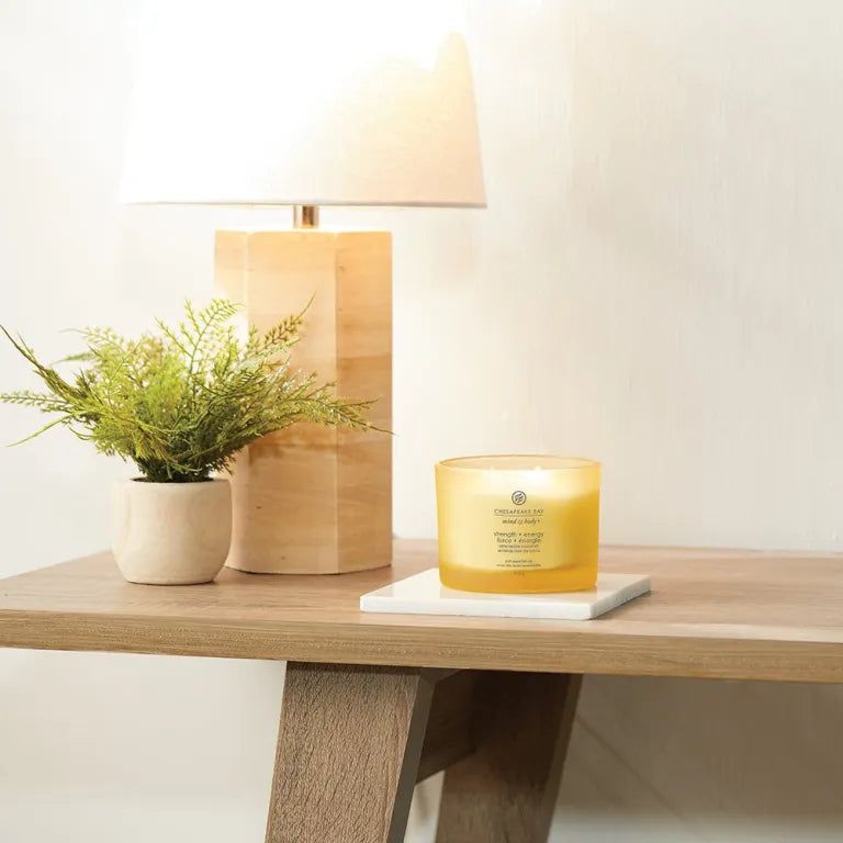 Bougie jaune sur une table, à côté d'une lampe et d'une plante en pot. Inscription: 'Chesapeake Bay Mind & Body'.