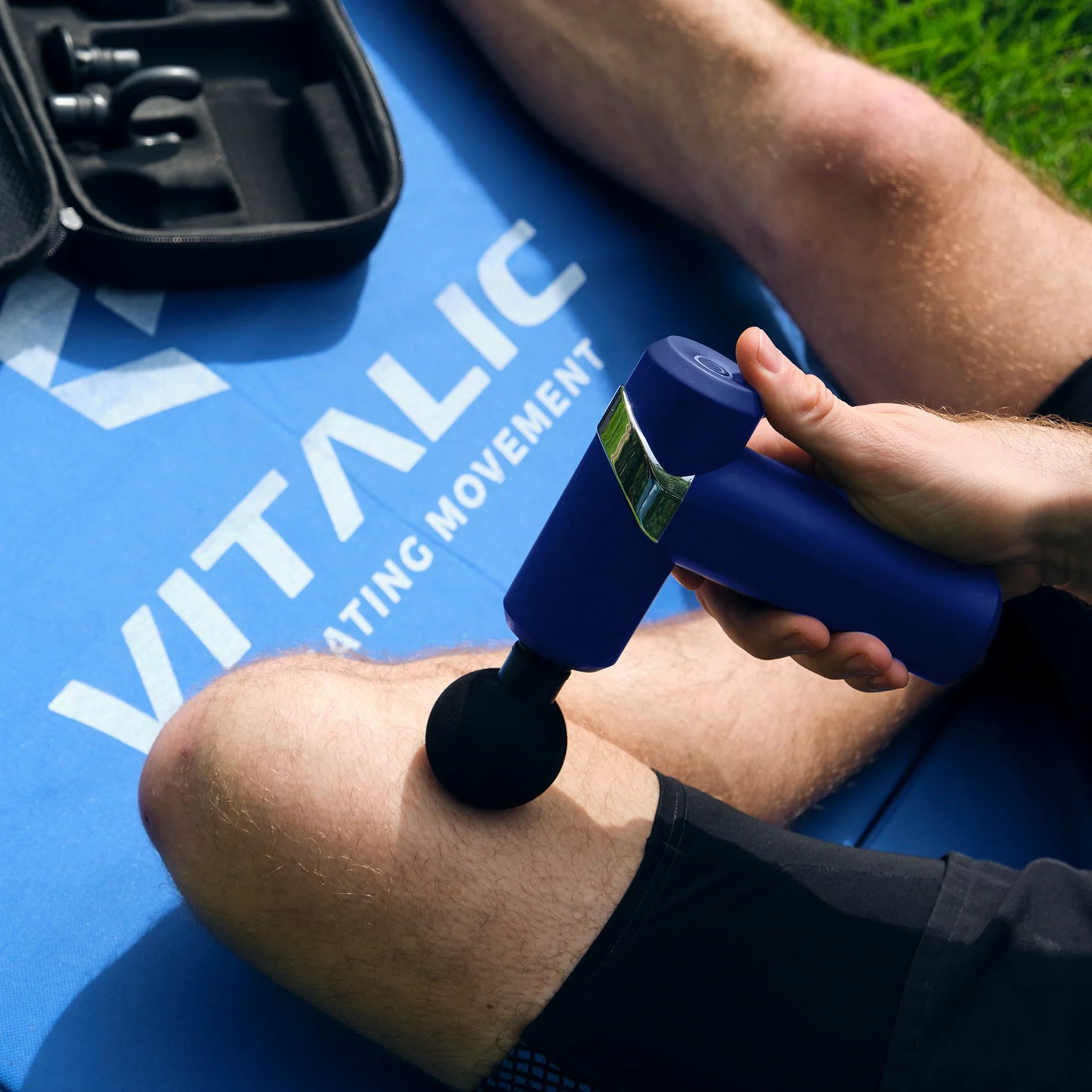 Personne utilise un pistolet de massage bleu sur la jambe. Logo VITALIC sur le tapis.