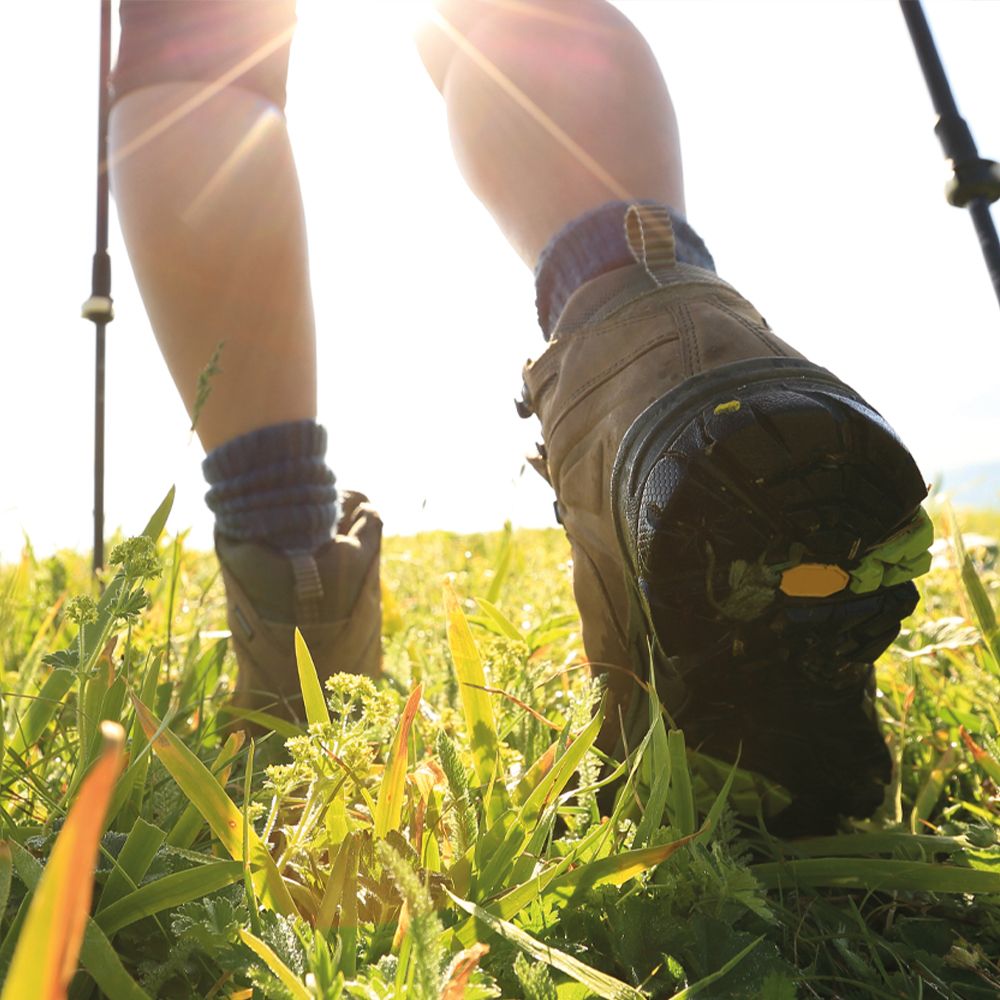 Personne en chaussures de randonnée marchant dans l'herbe. Lumière du soleil en arrière-plan. Chaussures marron.