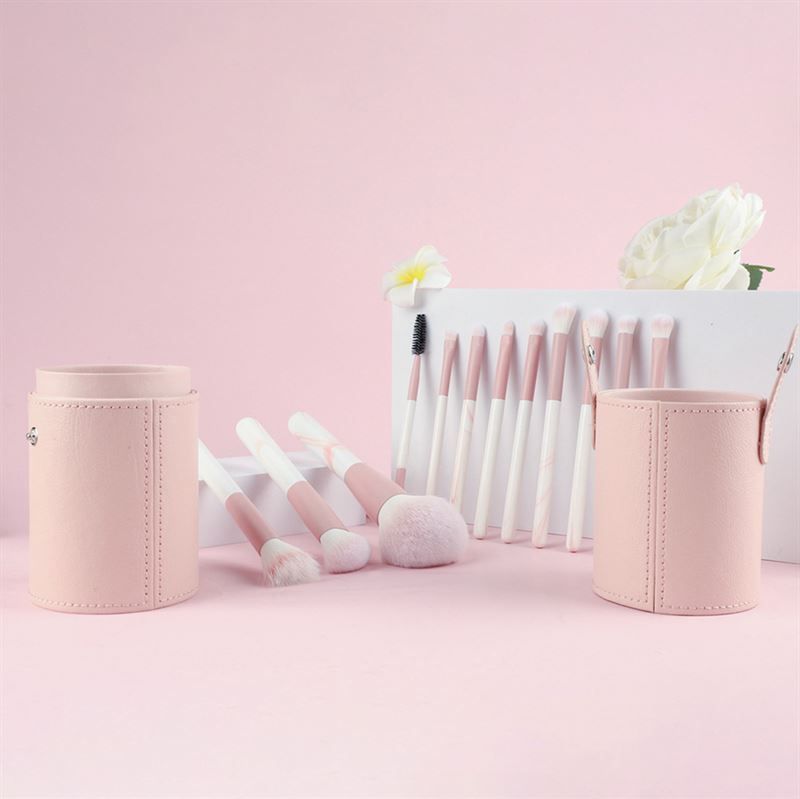 Ensemble de pinceaux de maquillage avec étuis roses. Pinceaux avec manches roses et blancs. Différentes formes et tailles. Placé sur une surface rose.