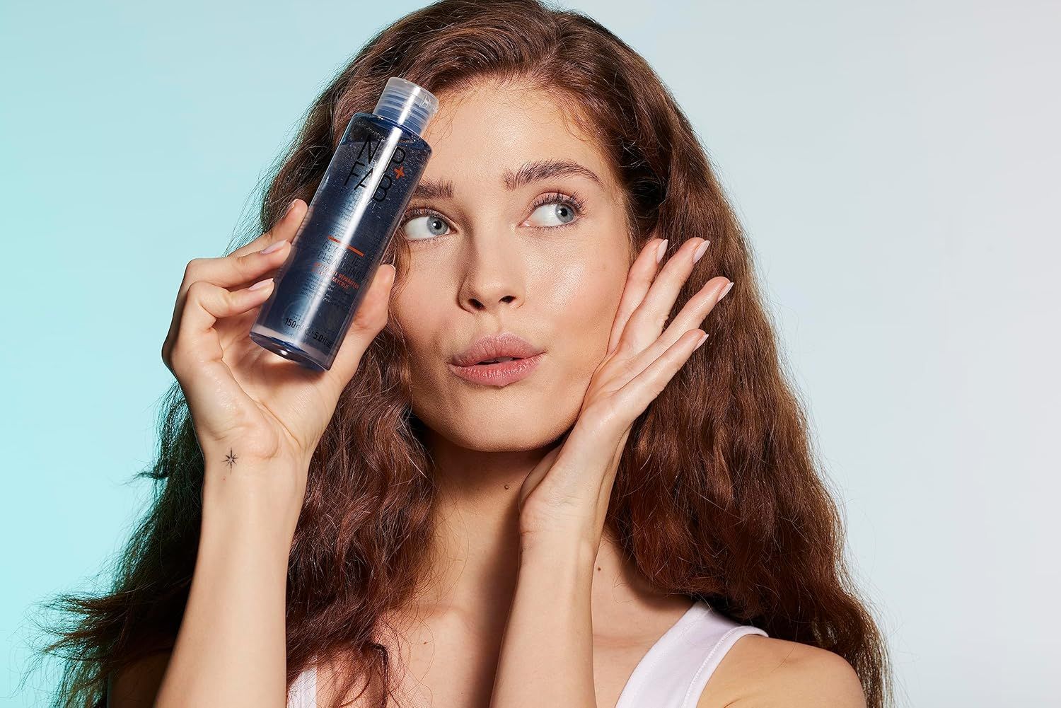 Vrouw houdt een fles Nip+Fab Glycolic Fix Cleanser vast. Blauwe vloeistof, transparante fles, witte dop.