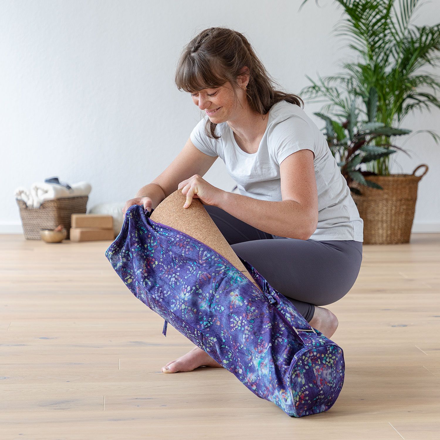 Vrouw opent yogatas, paars met patroon. Yogamat binnenin. Houten vloer.
