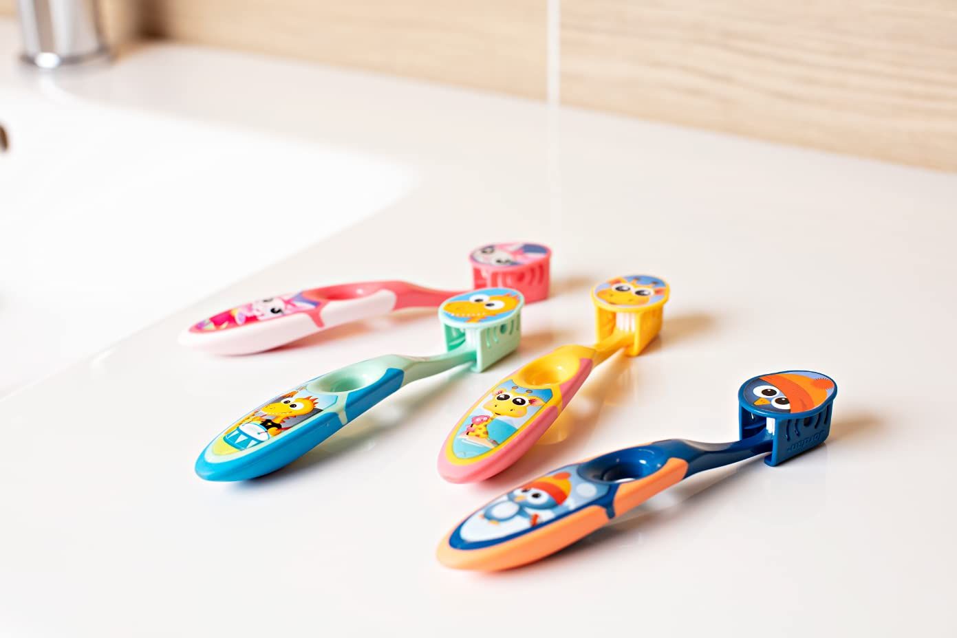 Cinq brosses à dents pour enfants aux manches colorés, motifs animaux, sur un lavabo.