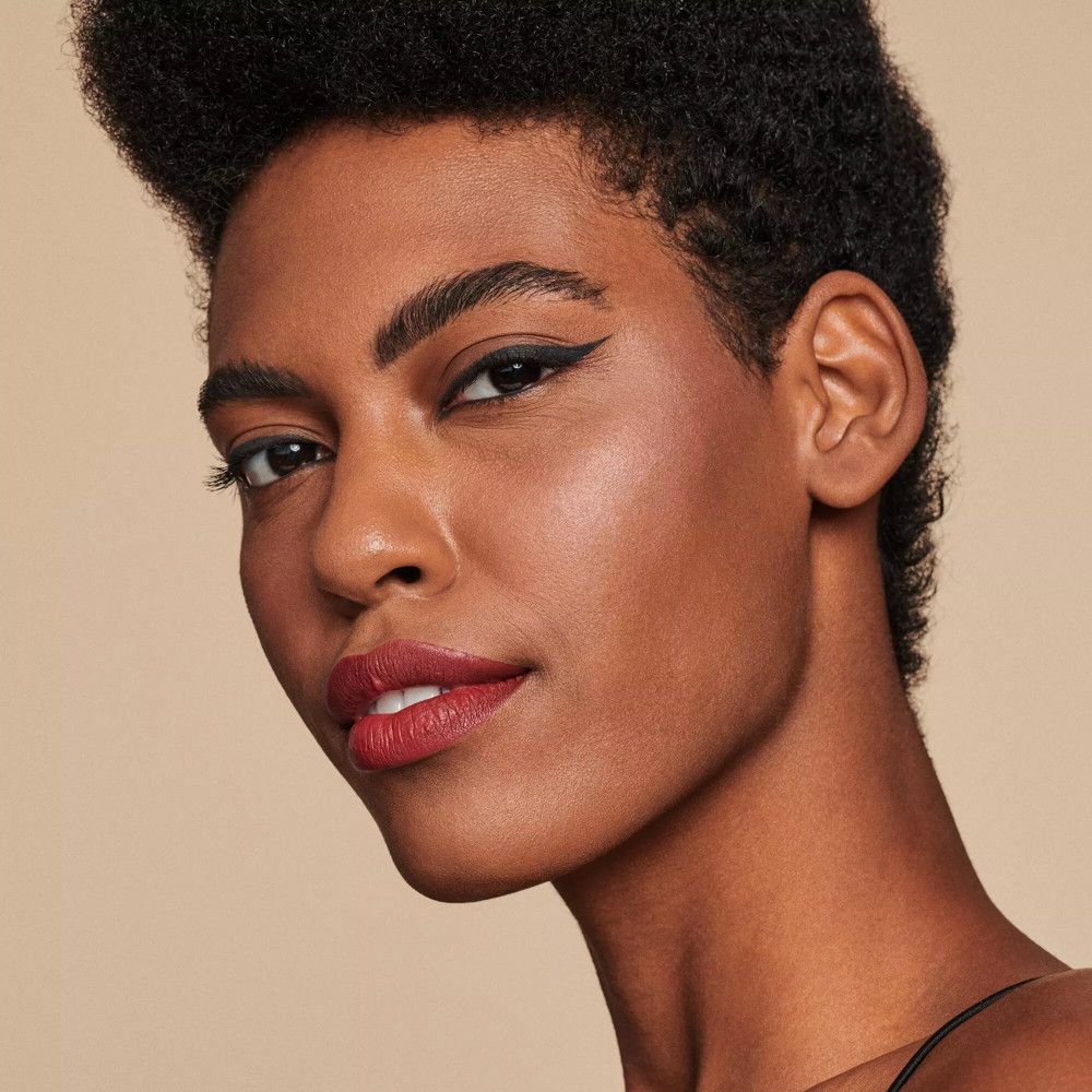 Portrait d'une femme à la peau foncée. Elle porte un eye-liner noir et un rouge à lèvres rouge foncé.