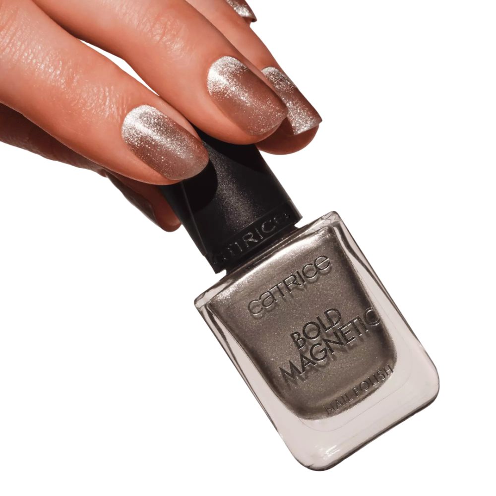 Main avec ongles vernis et flacon de vernis à ongles. Inscription : Catrice, Bold Magnetic, Nail Polish. Flacon incliné.
