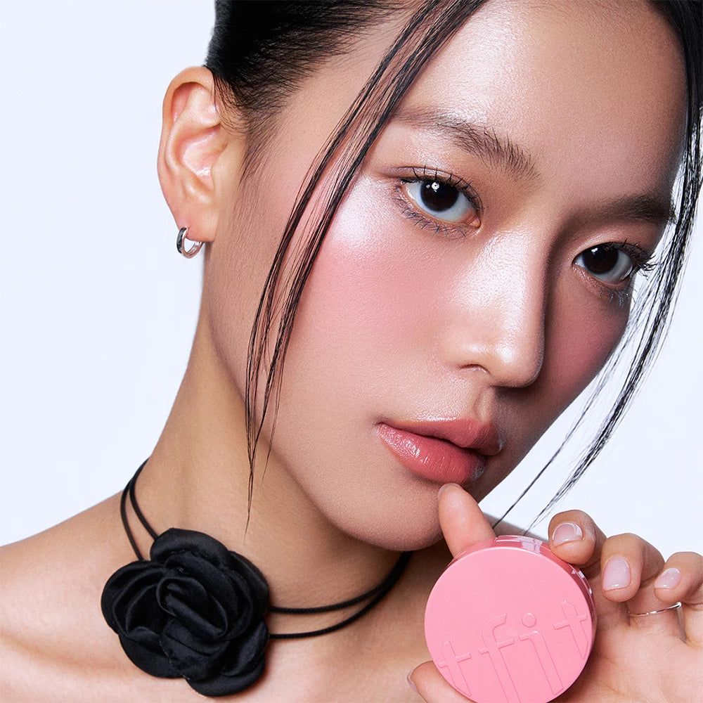 Portrait d'une femme avec du blush rose sur les joues. Elle tient un blush compact rose. Collier noir avec fleur.