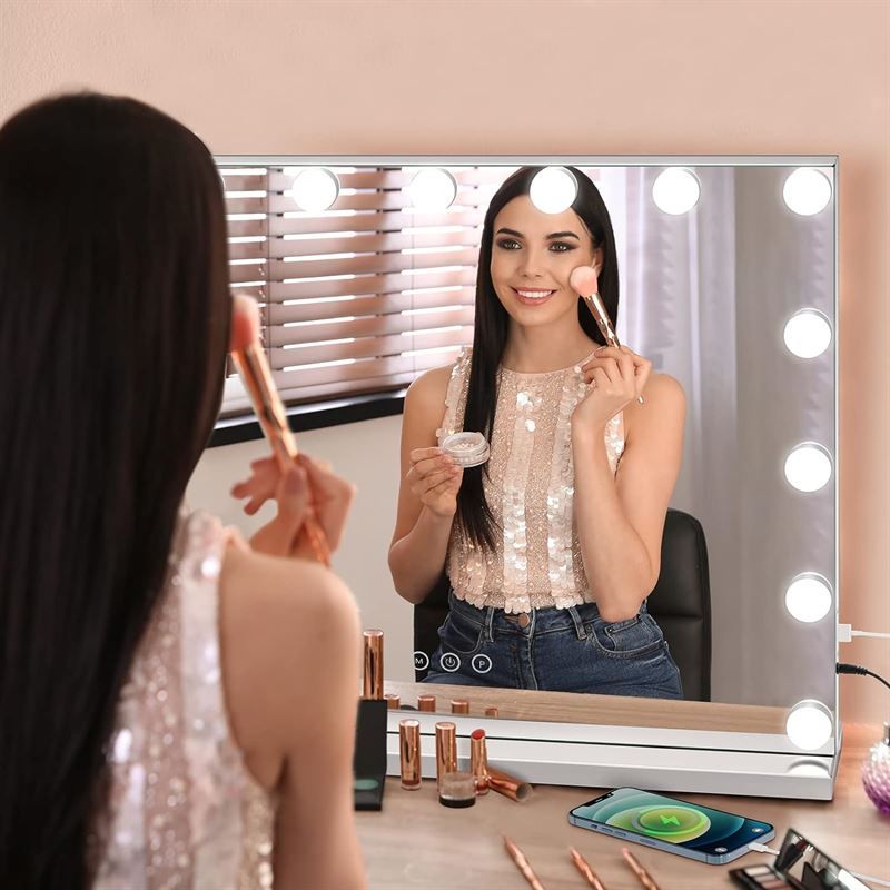 Femme se maquillant devant un miroir éclairé. Miroir avec lumières, femme tenant pinceau et poudre, accessoires de maquillage.