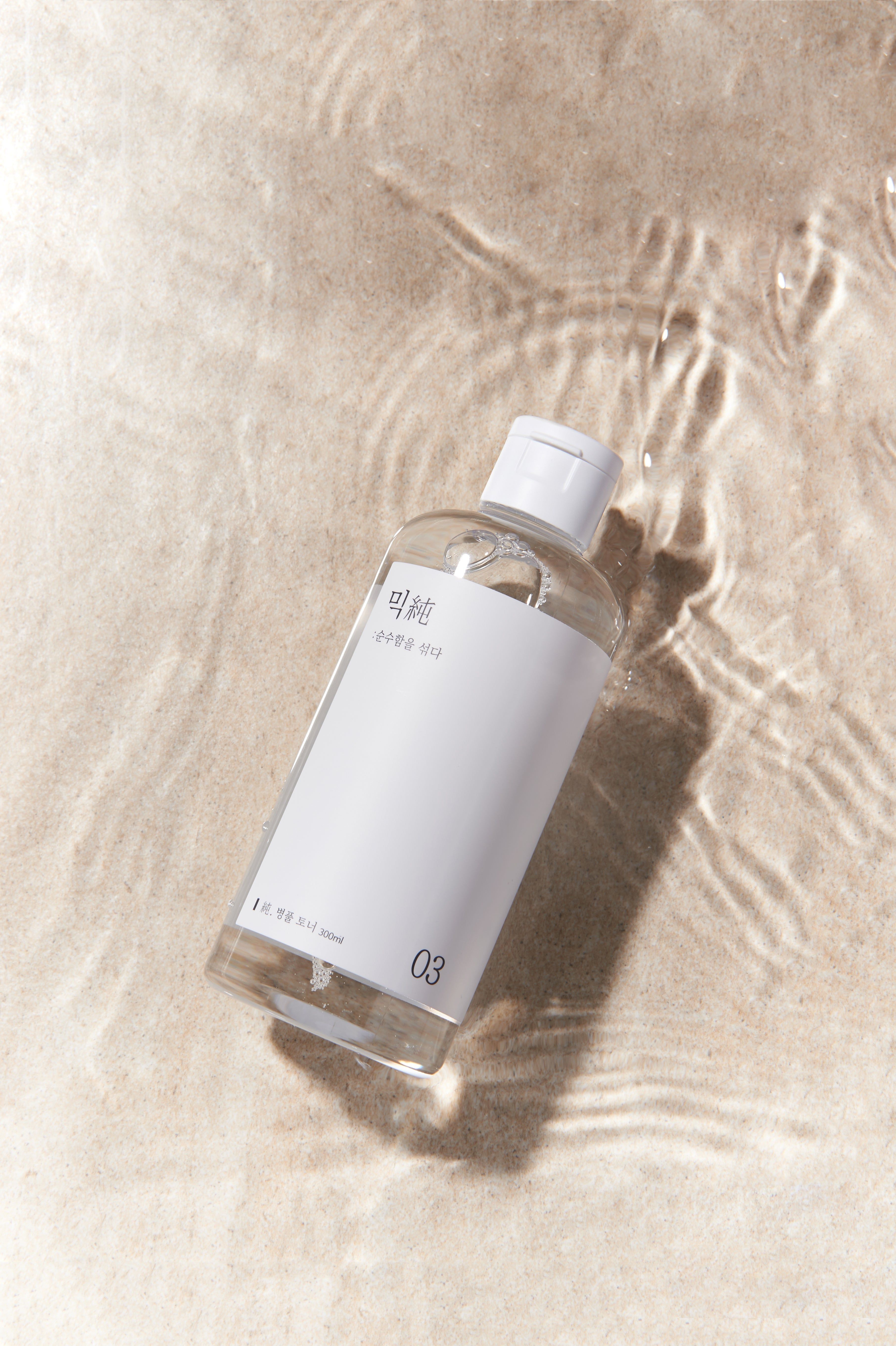 Flacon transparent avec bouchon blanc et étiquette, dans l'eau. Inscription en coréen et le chiffre 03. Inscription: 200ml.
