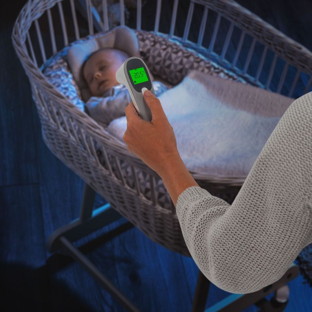 Thermomètre infrarouge mesurant la température d'un bébé endormi. Le thermomètre affiche 36,5°C. Marque : reer.