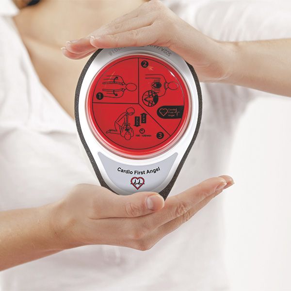 Cardio First Angel tenu par des mains. Bouton rouge avec instructions, cadre blanc, mousse grise. Texte: Cardio First Angel.