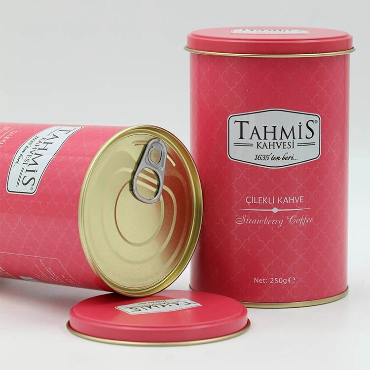 Twee rode blikken 'Tahmis Kahvesi'. Eén geopend, deksel ernaast. Tekst: 'Çilekli Kahve Strawberry Coffee'.