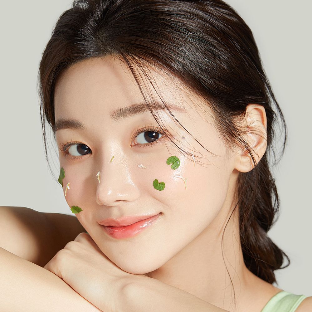 Portret van een vrouw met transparant product en groene blaadjes op de huid. Ze lacht in de camera.