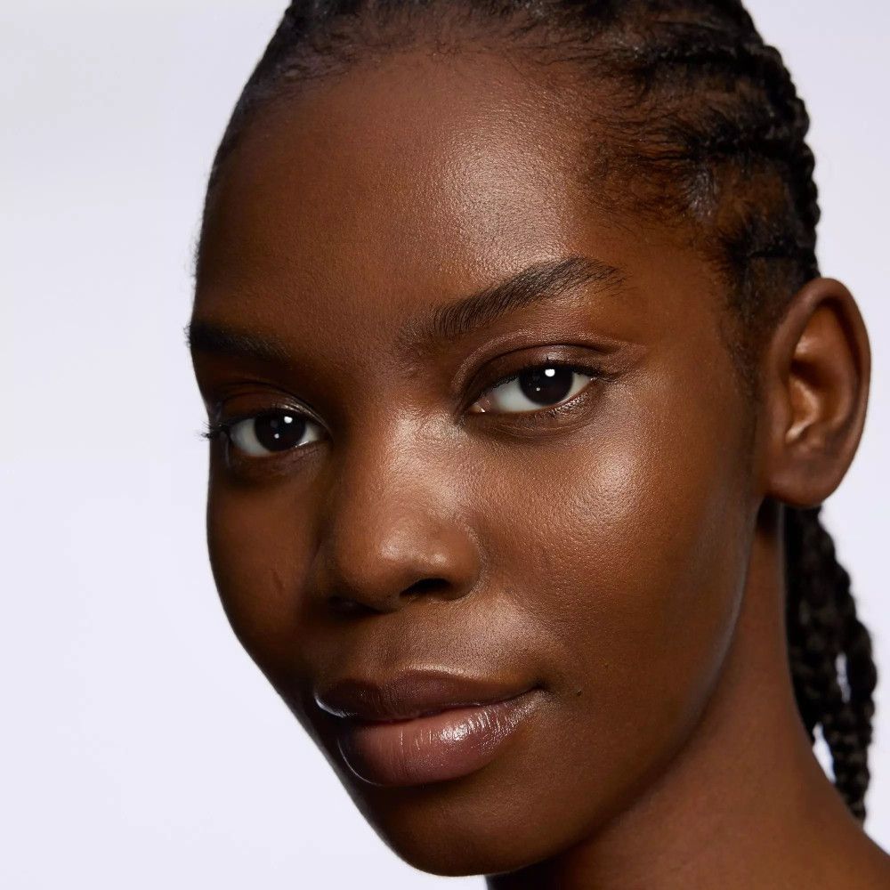 Gros plan d'une femme à la peau foncée et aux cheveux tressés. Elle porte du maquillage.