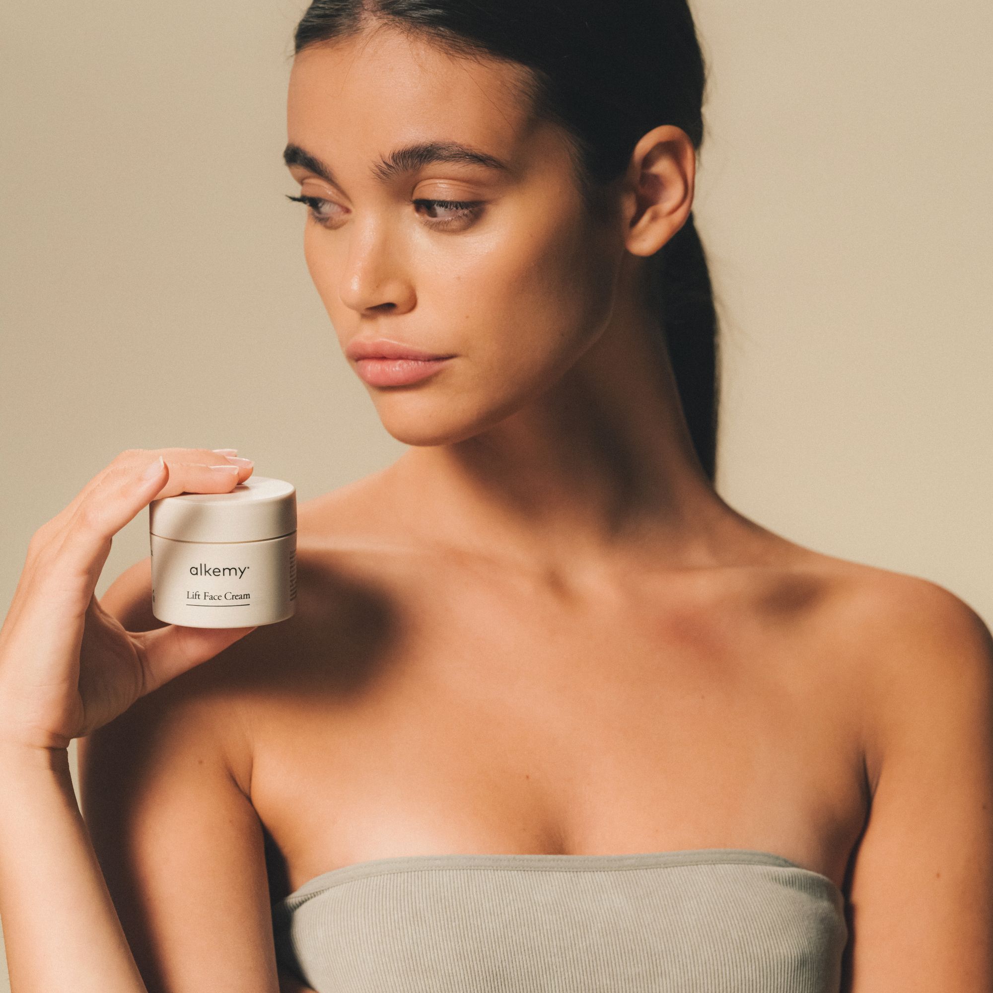 Vrouw die een pot Alkemy Lift Face Cream vasthoudt, tekst: Zorg voor je huid.