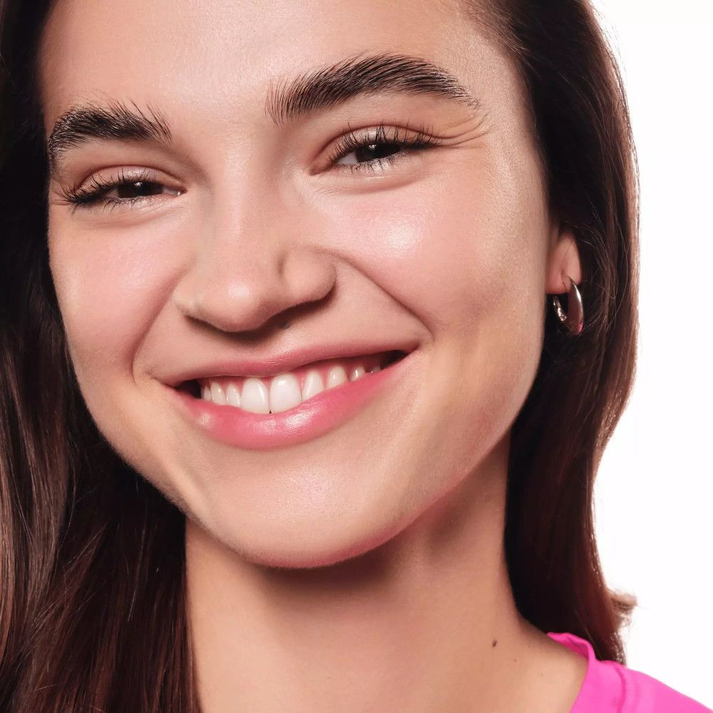 Gros plan d'une femme souriante avec des boucles d'oreilles. Elle porte un haut rose.