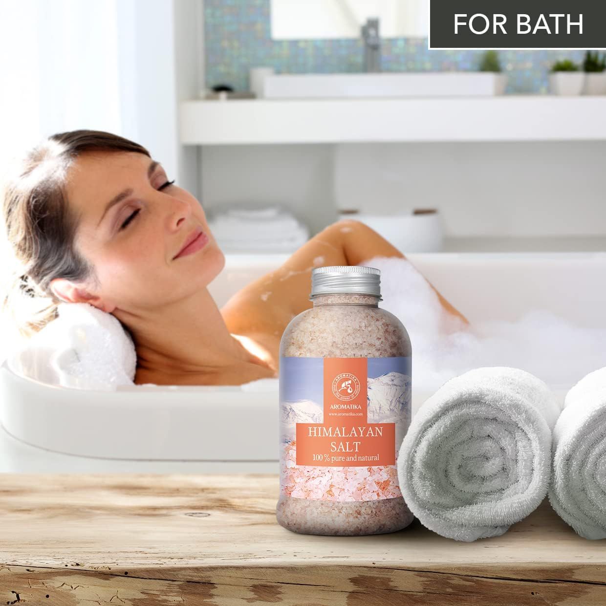 Une femme se détend dans une baignoire avec une bouteille de sel d'Himalaya et deux serviettes roulées à côté.