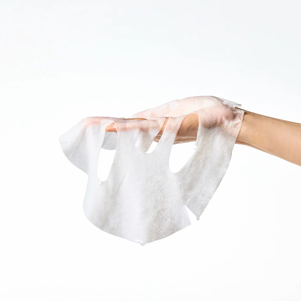 Une main tient un masque facial blanc. Le masque a des ouvertures pour les yeux, le nez et la bouche. Le fond est blanc.
