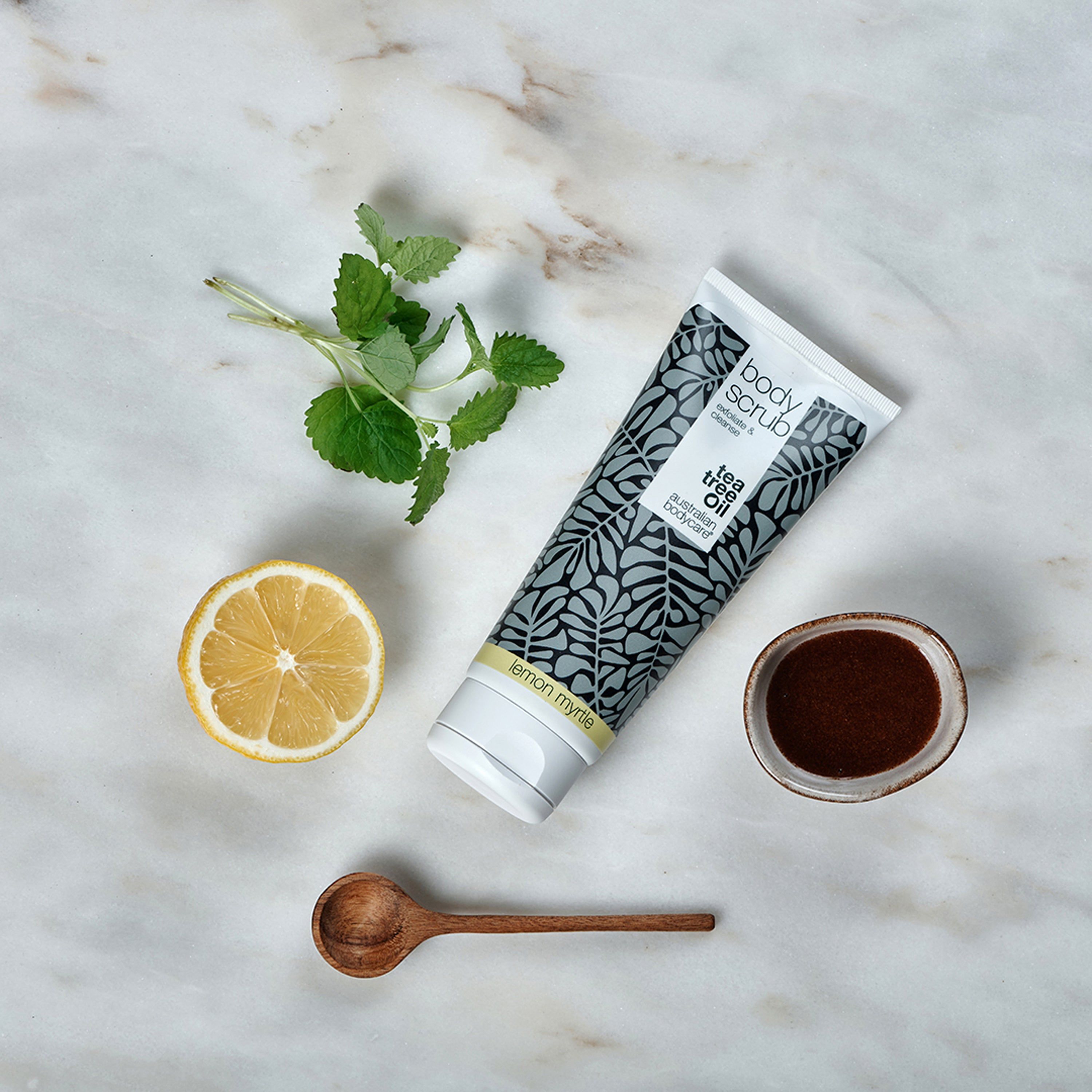 Tube de gommage corporel, citron, menthe et cuillère en bois sur marbre. Inscription : Body Scrub, Australian Bodycare.
