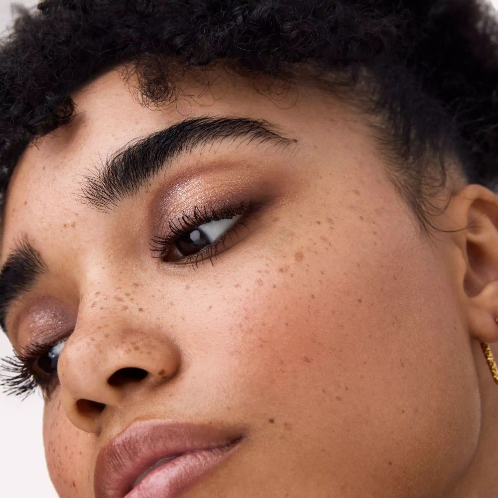 Gros plan d'un visage avec les yeux maquillés. Peau bronzée, taches de rousseur, sourcils et cils foncés.