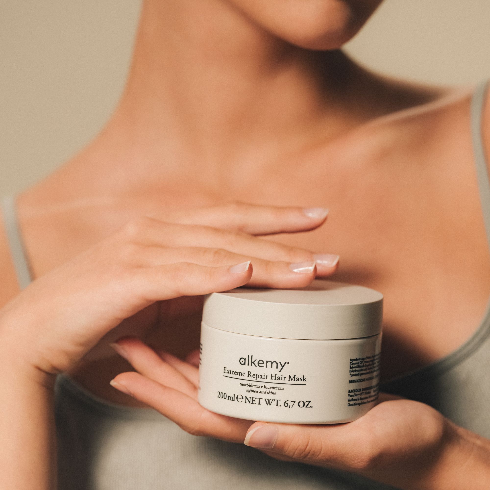 Une femme tenant un pot de Masque Capillaire Réparateur Intense Alkemy.