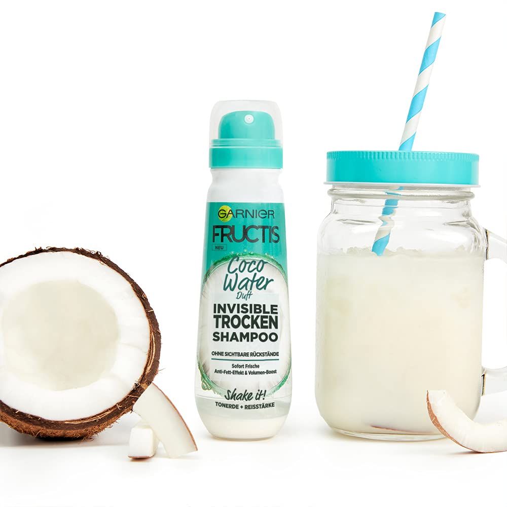 Shampooing sec Garnier Fructis, noix de coco, boisson avec paille. Produit à côté de morceaux de noix de coco.