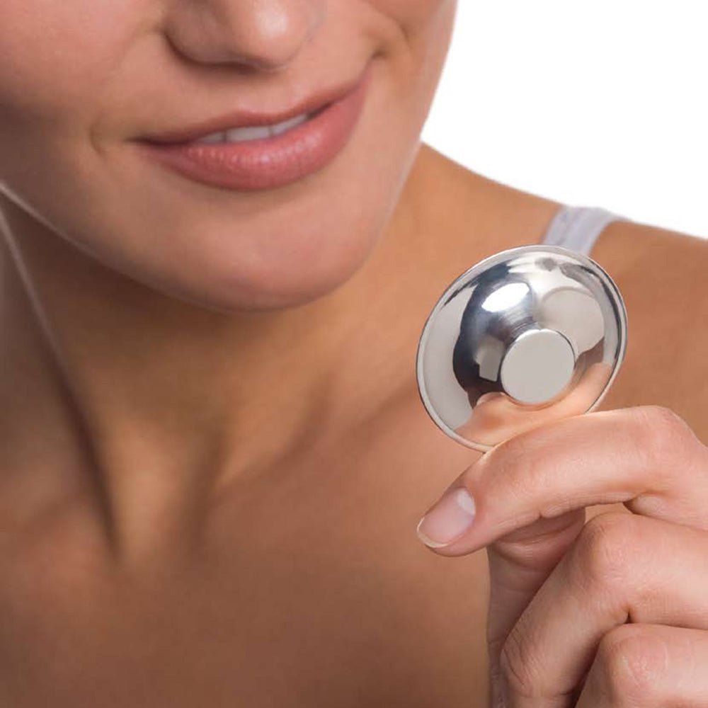 Protection d'allaitement argentée, tenue par une personne. Forme ronde avec partie centrale surélevée.