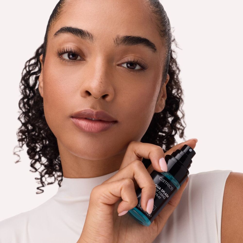 Femme tenant un flacon spray noir avec liquide bleu. Inscription: Catrice, Aqua Splash Grip Fixing Spray. Hydratant.
