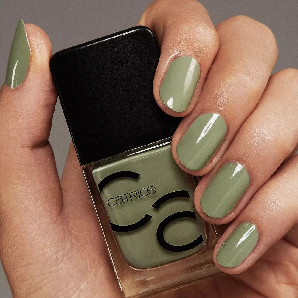 Main avec ongles vernis et flacon de vernis à ongles. Les ongles sont peints en vert. CATRICE est écrit sur le flacon.