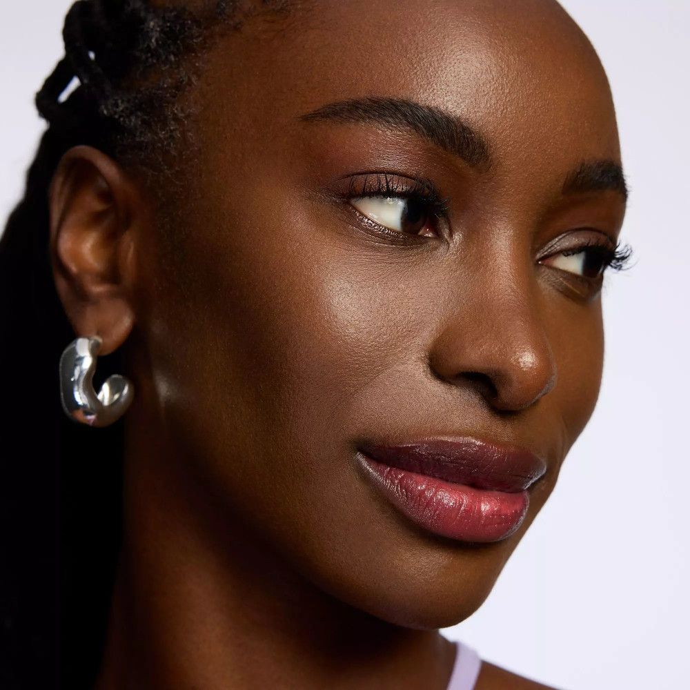 Portrait d'une femme avec du baume à lèvres. Les lèvres sont rouge foncé. Elle porte des boucles d'oreilles argentées.