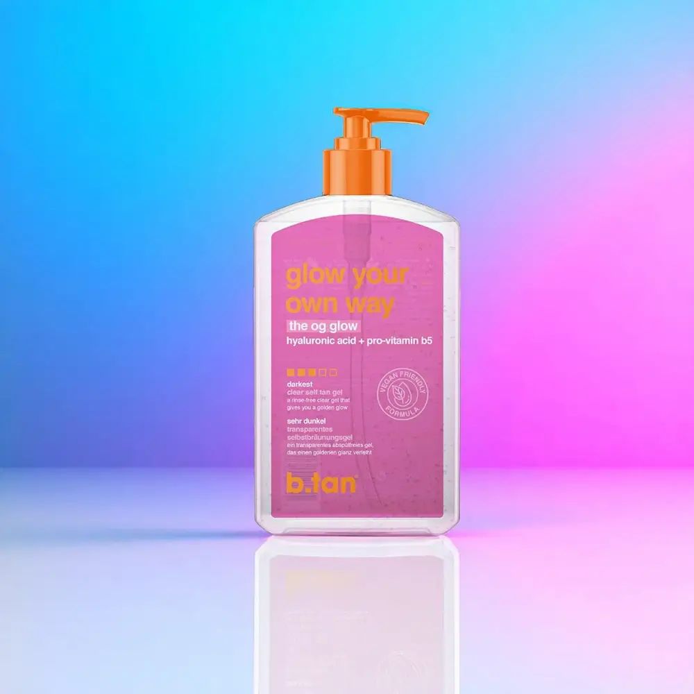 Flacon transparent avec étiquette rose. Inscriptions : "glow your own way", "the og glow", "b.tan". Sceau végétalien. Pompe orange.