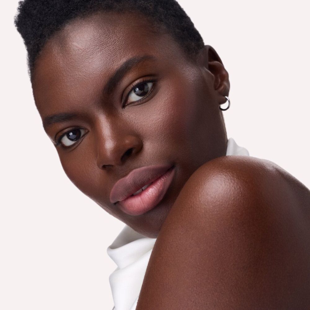 Portrait d'une femme à la peau foncée. Les lèvres sont mises en valeur avec un rouge à lèvres rosé.