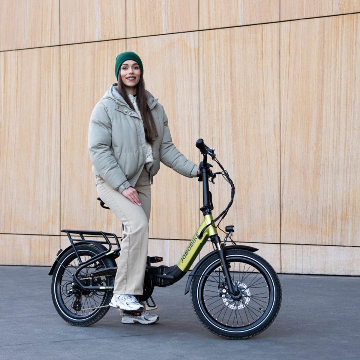 Vélo électrique pliable vert et noir. Logo JOBOBIKE. Porte-bagages, garde-boue. Personne en vêtements d'hiver.