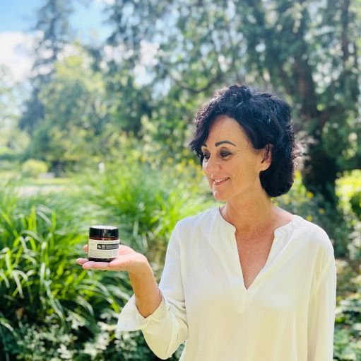 Femme tenant un pot en verre brun. Arrière-plan : nature. Logo oxy8 Naturkosmetik.